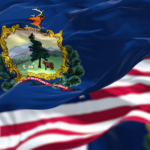 Vermont State Flag on a flag pole blowing in the wind, with the American Flag behind it.