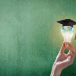 Hand holding an illuminated lightbulb wearing a graduation cap with a green background