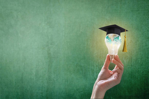 Hand holding an illuminated lightbulb wearing a graduation cap with a green background