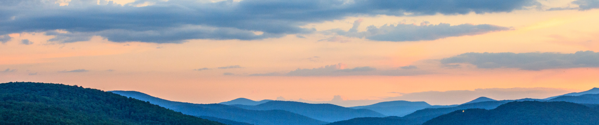 A beautiful mountain scape of blue mountains with a peachy sky with dark clouds in the background