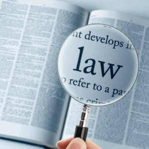 A person is holding a magnifying glass over a book with tiny print and the only thing in focus is within the glass--it says "law"