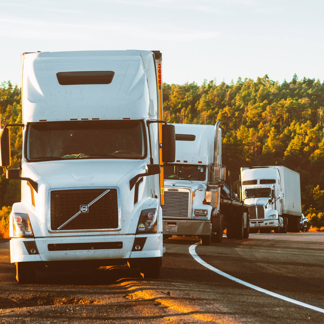 Stock image of a line of 3 trucks driving on the road at sunset
